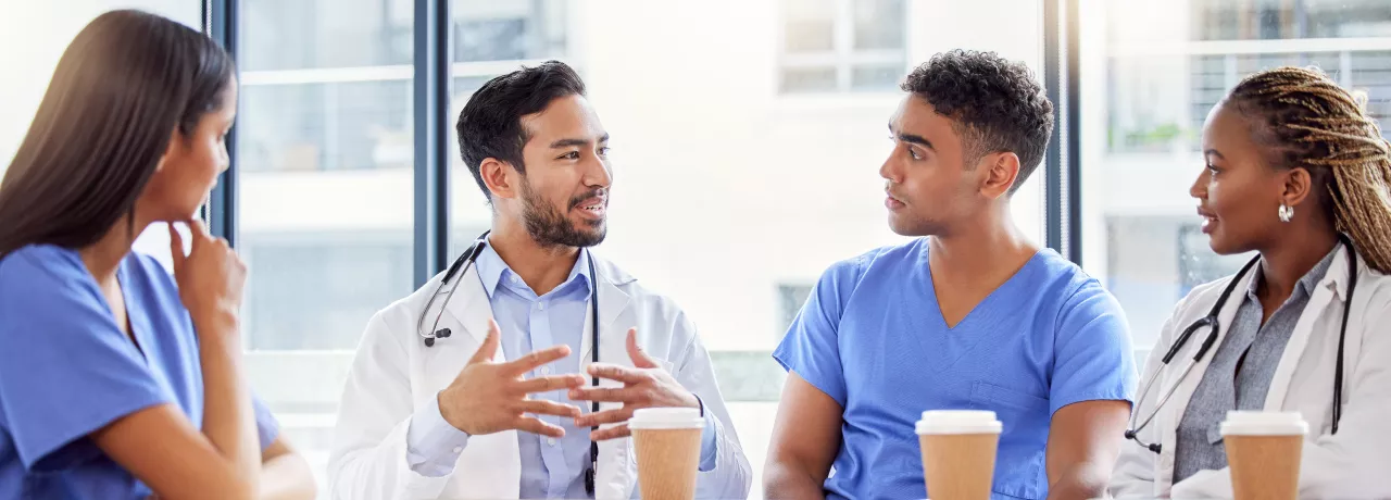 Two doctors and two nurses chatting at a table with coffee 