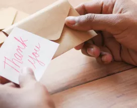 Image shows a person putting a note that says "thank you" into an envelope