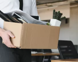 Image shows a person leaving an office with a box of items.