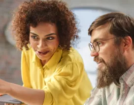 An employee training a new hire in front of a computer as part of their onboarding strategy
