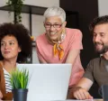 Four employees in varying generations working together at a computer at work.
