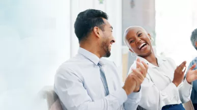 Image shows two employees laughing together along with two others in the background.