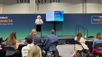 Image shows Theresa Harkins-Schulz, Inspirus SVP of Product and Customer Experience, speaking at the Total Rewards conference in front of attendees.