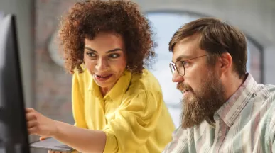 An employee training a new hire in front of a computer as part of their onboarding strategy